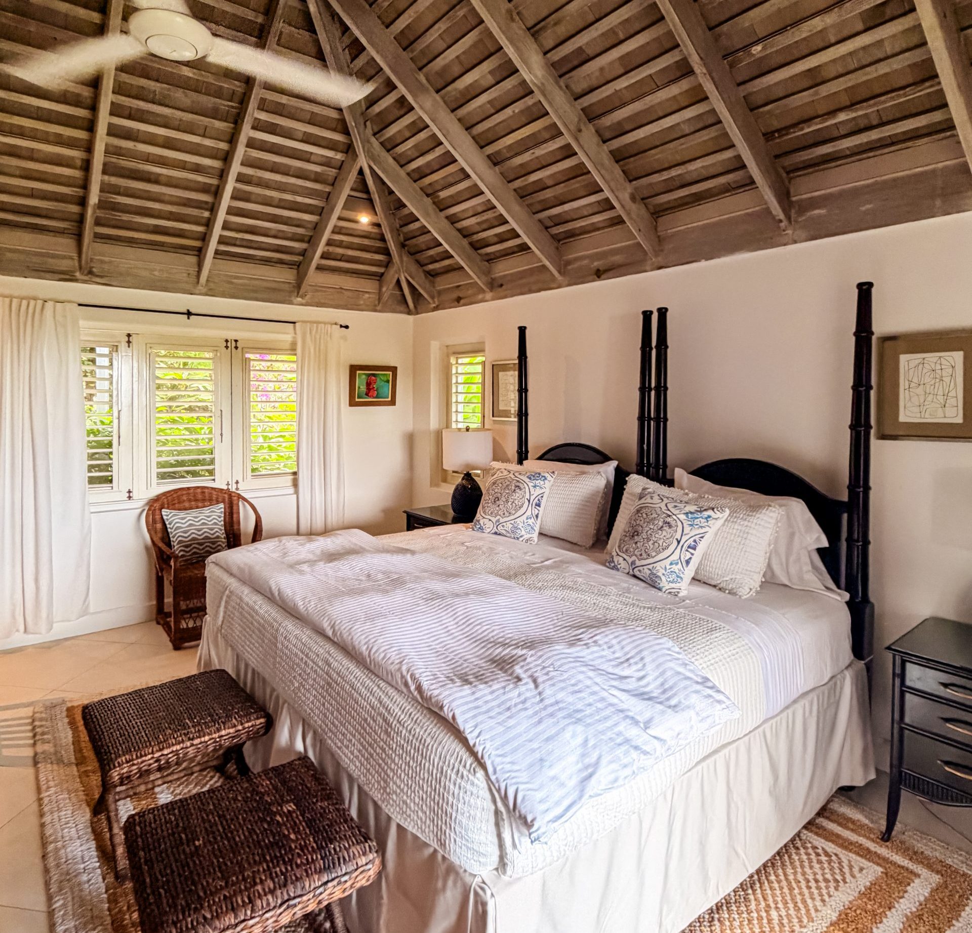 Blue Heron villa suite with vaulted wooden ceiling, queen bed, woven stools, and natural light at Coconut Cottage.