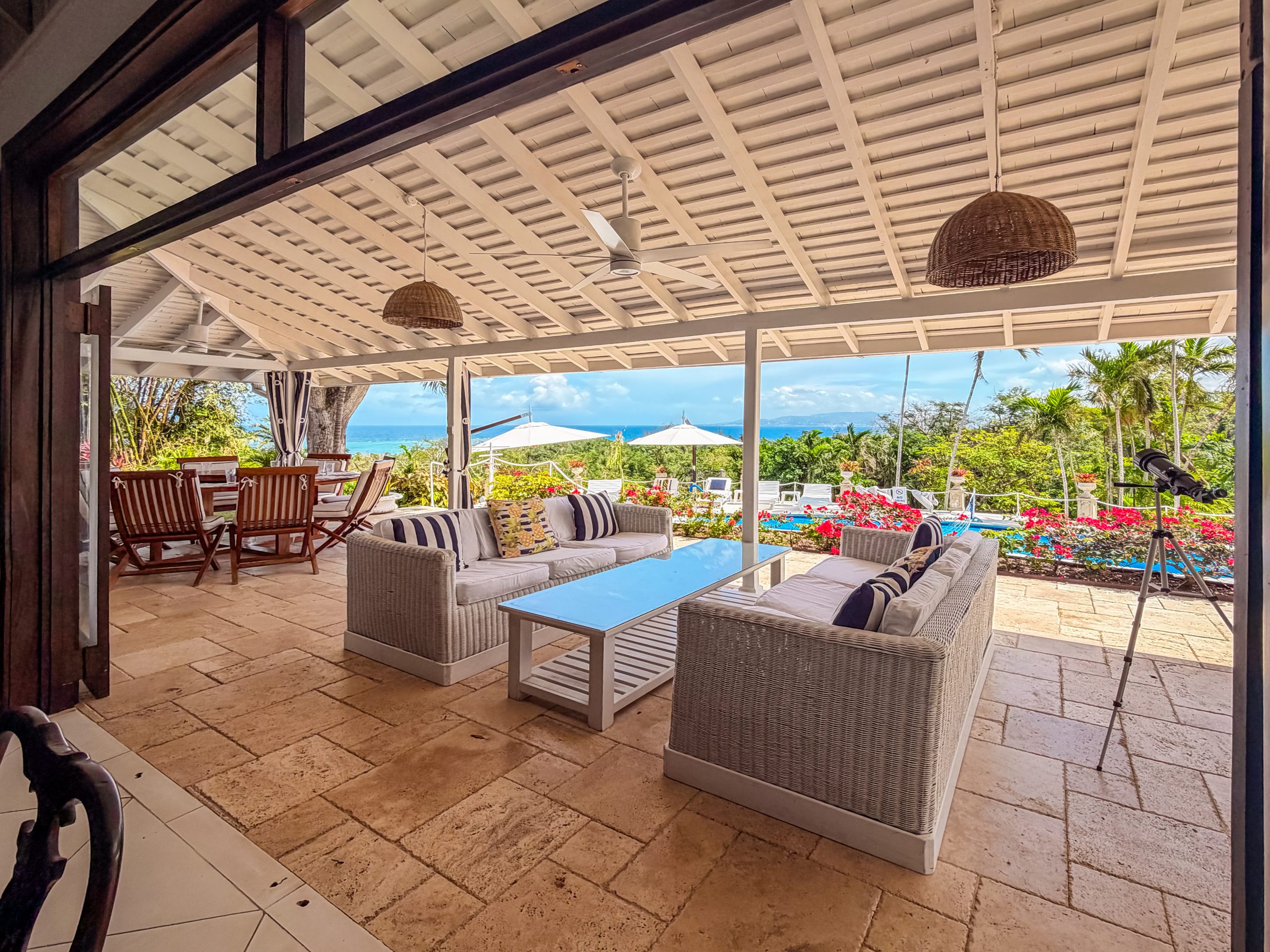 Open‑air veranda at Coconut Cottage with wicker seating, ocean views, tropical gardens, and a telescope overlooking Montego Bay.