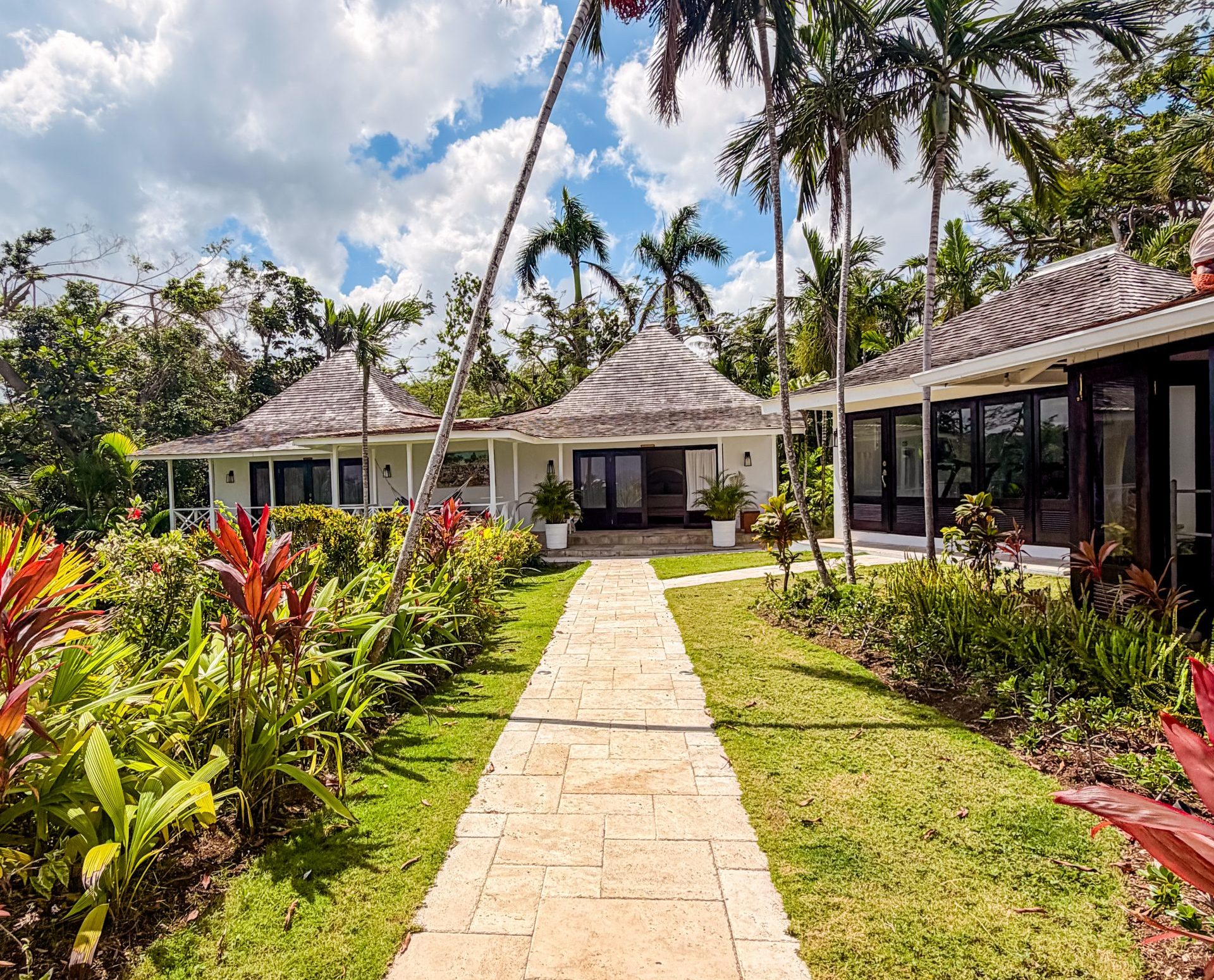 Tropical luxury villa with lush gardens, palm trees, and shingled rooftops at Coconut Cottage in Montego Bay.