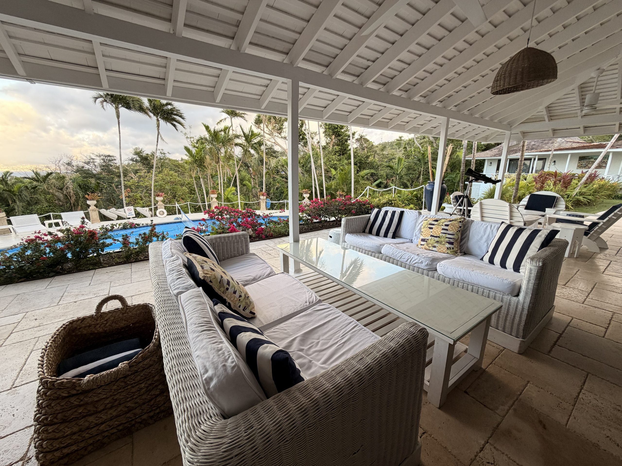 Outdoor verandah at Coconut Cottage Montego Bay with white wicker seating overlooking the pool, gardens and palm trees.