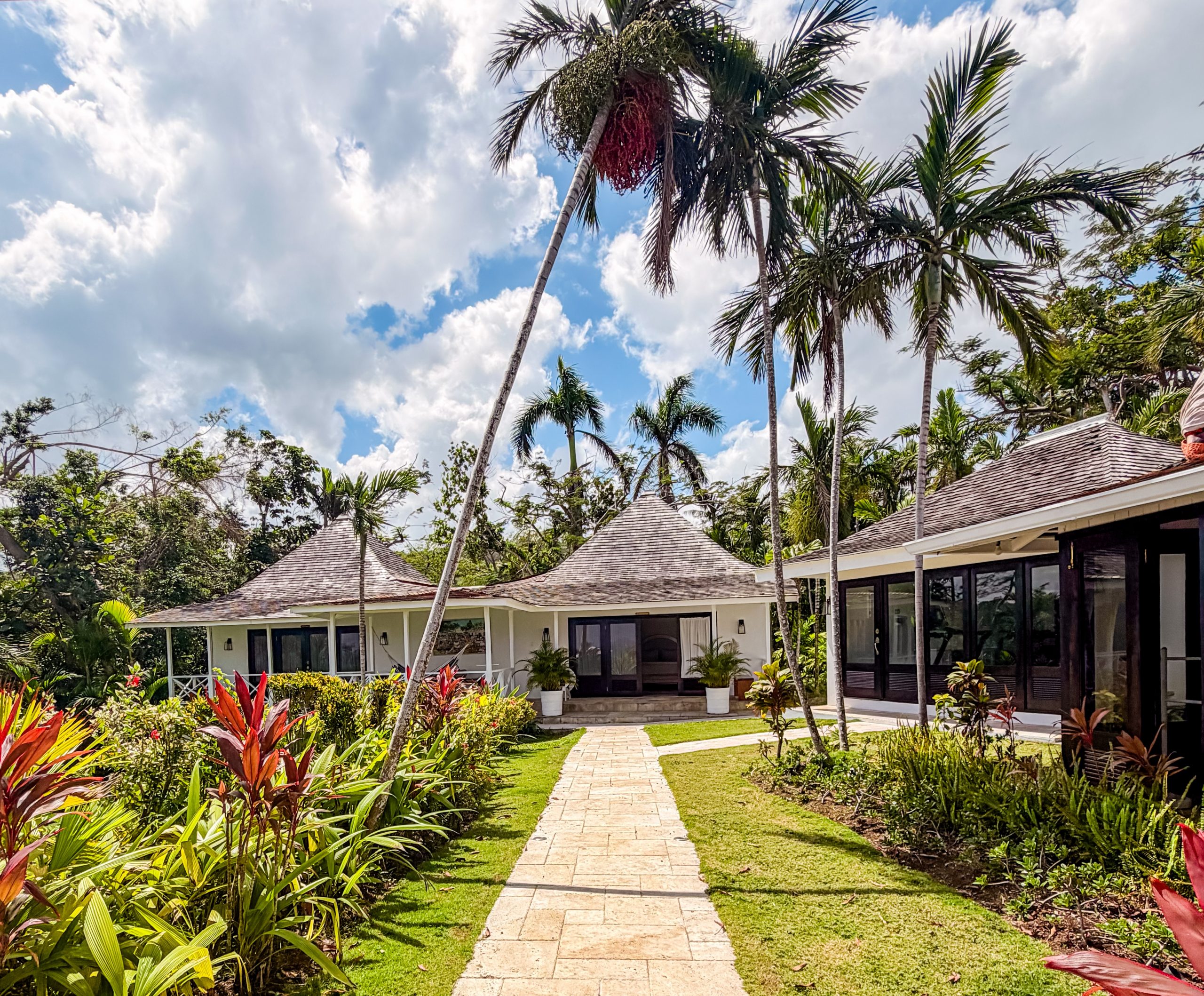 Tropical garden pathway at Coconut Cottage Montego Bay with shingled villa rooftops, palm trees and vibrant foliage.
