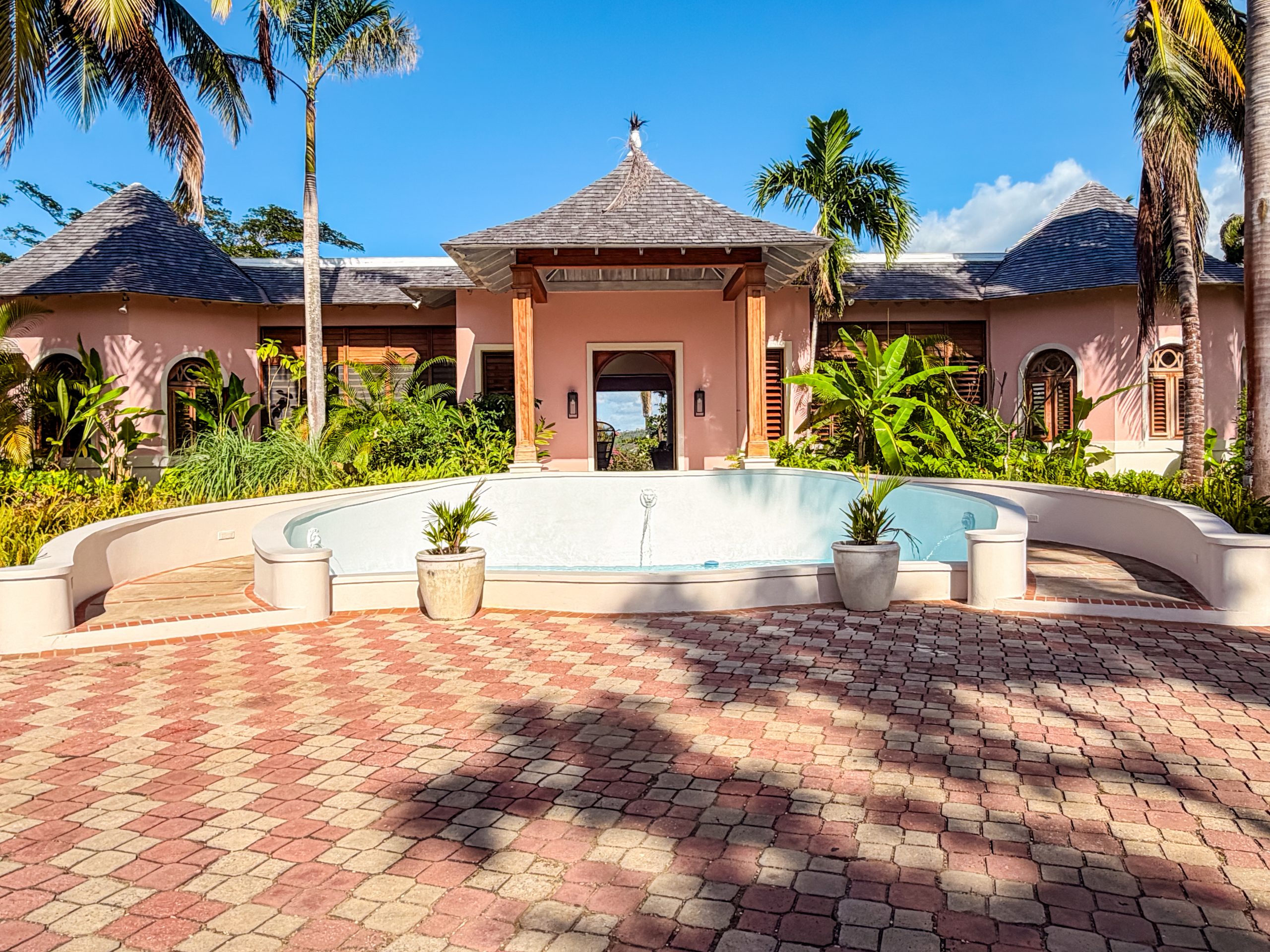 Tropical courtyard at The Tryall Club with pink villa, palm trees, and a circular fountain.