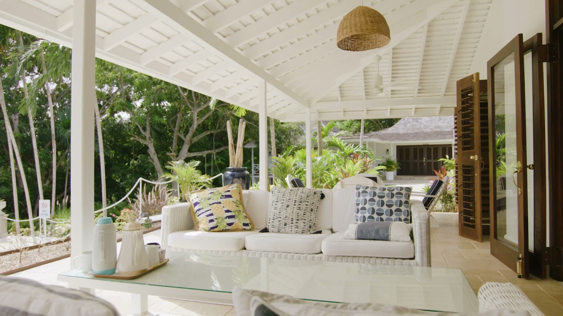 White outdoor lounge chairs with navy cushions on a sunlit patio surrounded by tropical plants at Coconut Cottage.