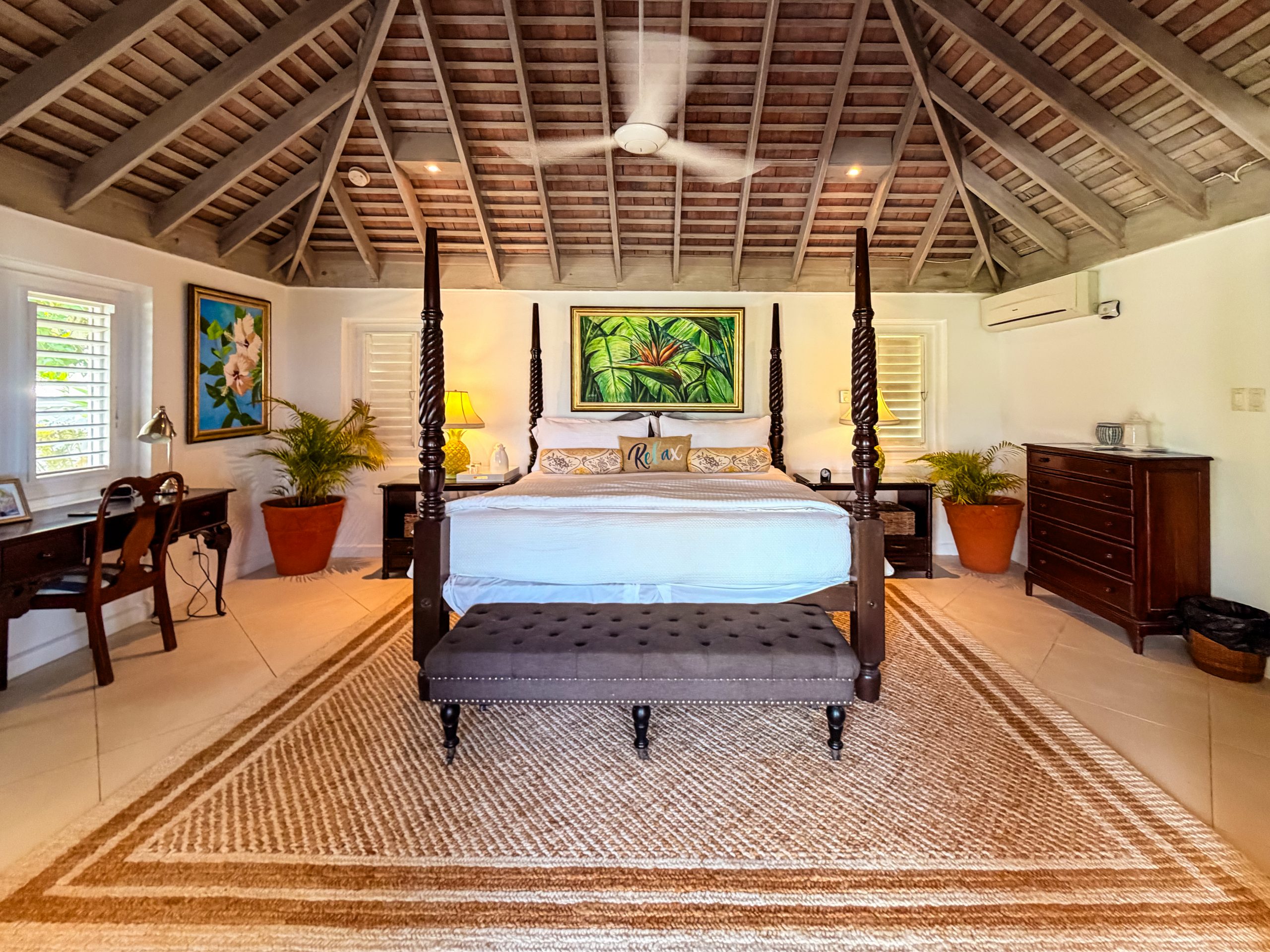Master suite at Coconut Cottage with a four‑poster bed, tropical décor and airy wooden ceilings.