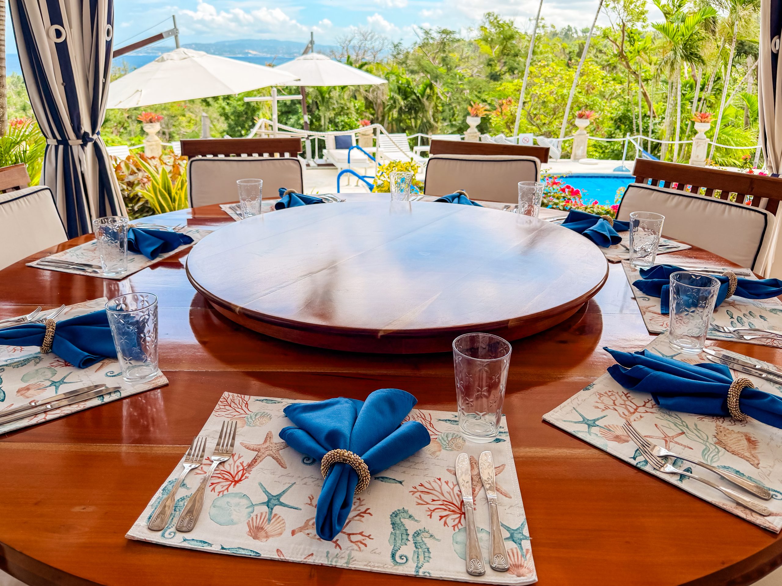 Outdoor dining table set for six overlooking the pool, tropical gardens and hillside views at Coconut Cottage villa in Montego Bay.