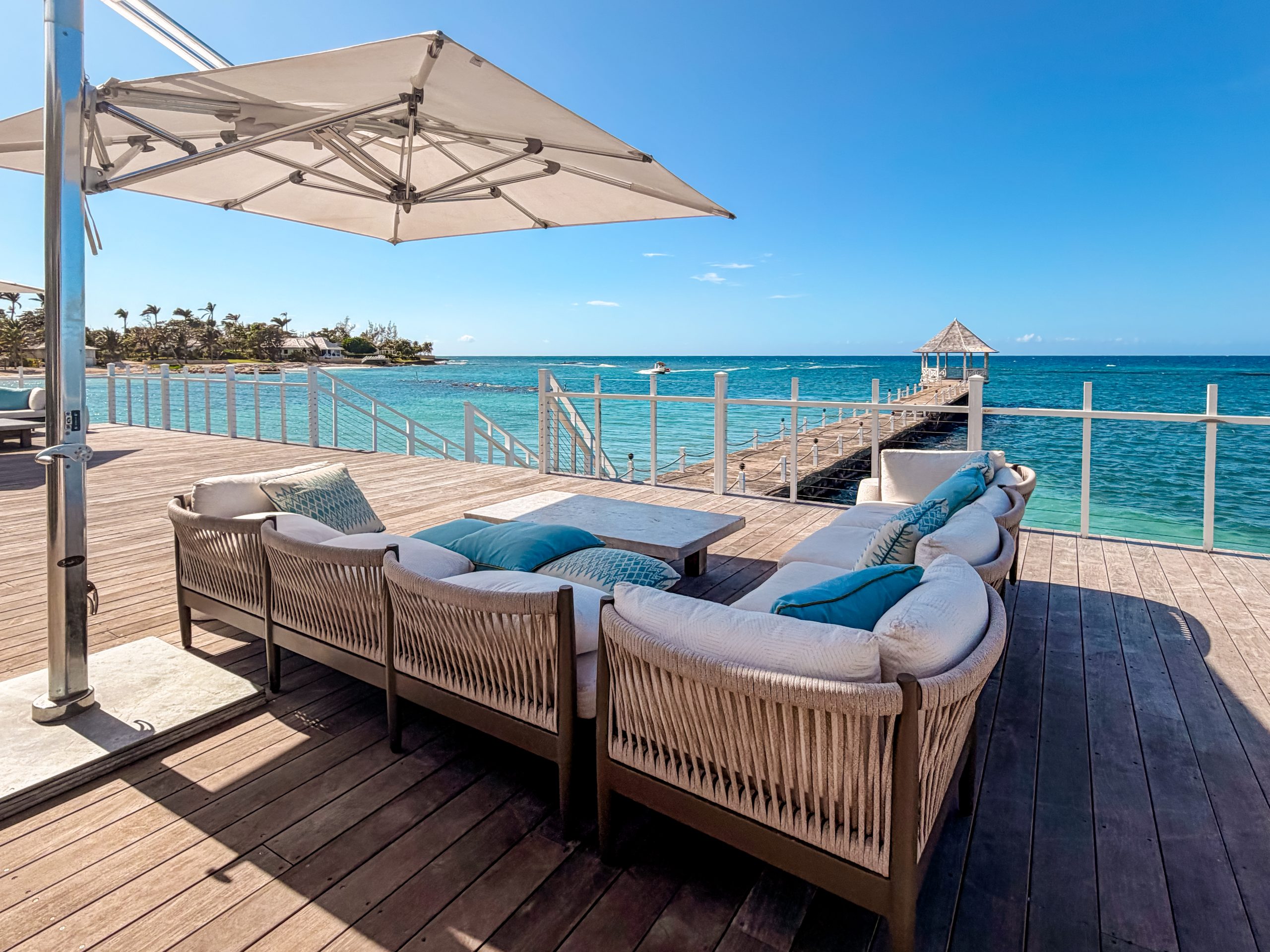 Oceanfront deck at the Tryall Club with cushioned loungers, umbrella shade and a long pier over turquoise water.