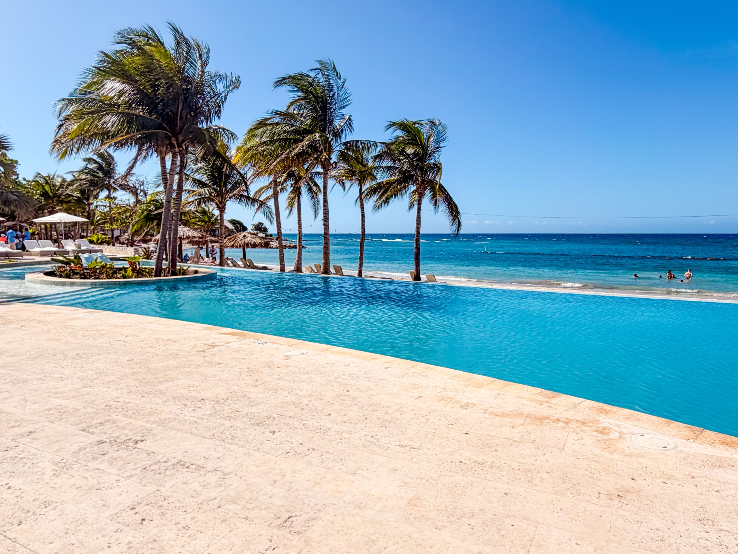 Infinity pool at the Tryall Club overlooking turquoise ocean water with palm trees and loungers.