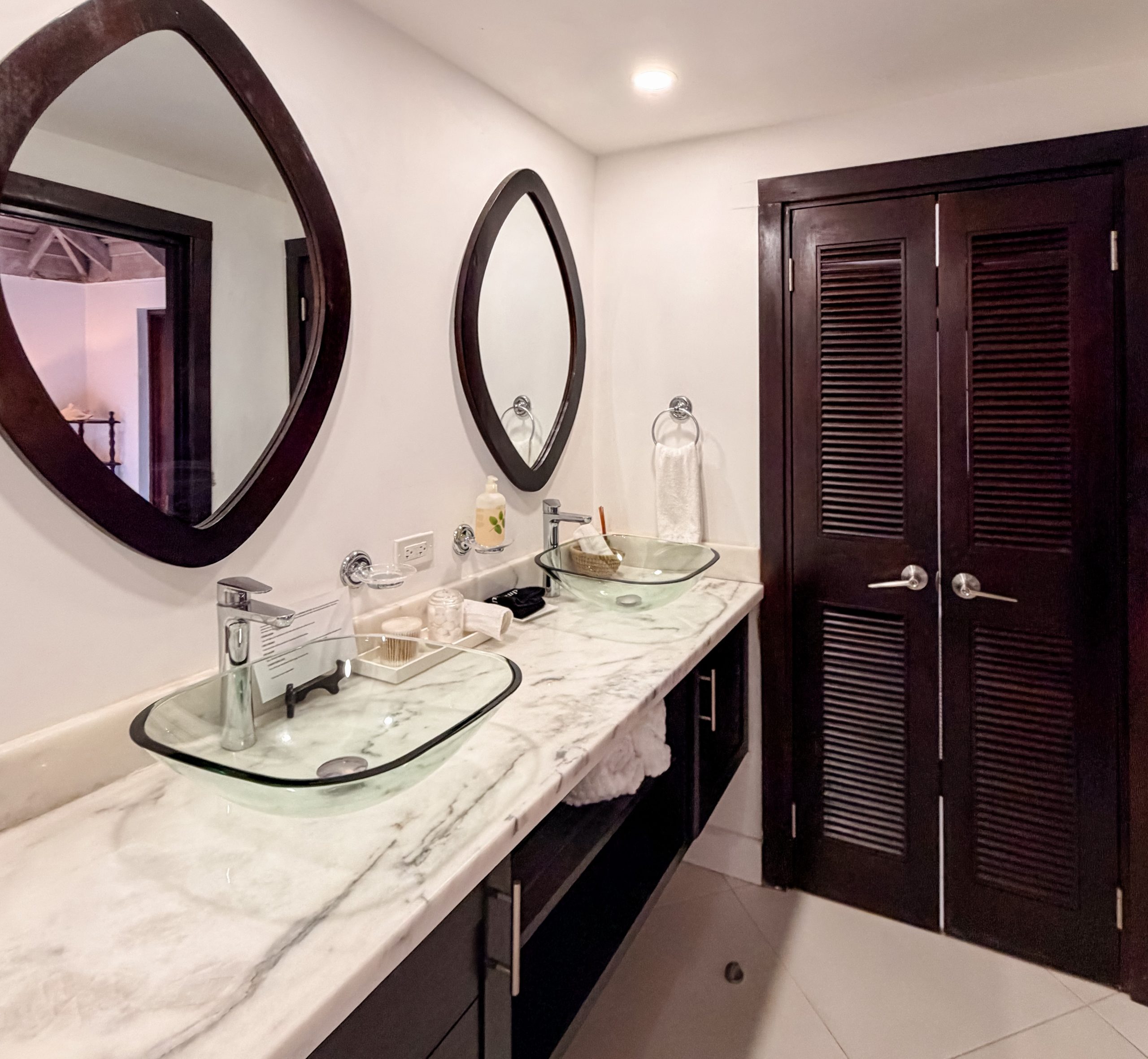 Luxury bathroom in the Magenta suite at Coconut Cottage with double vanity, glass vessel sinks, marble countertop and warm wood cabinetry.