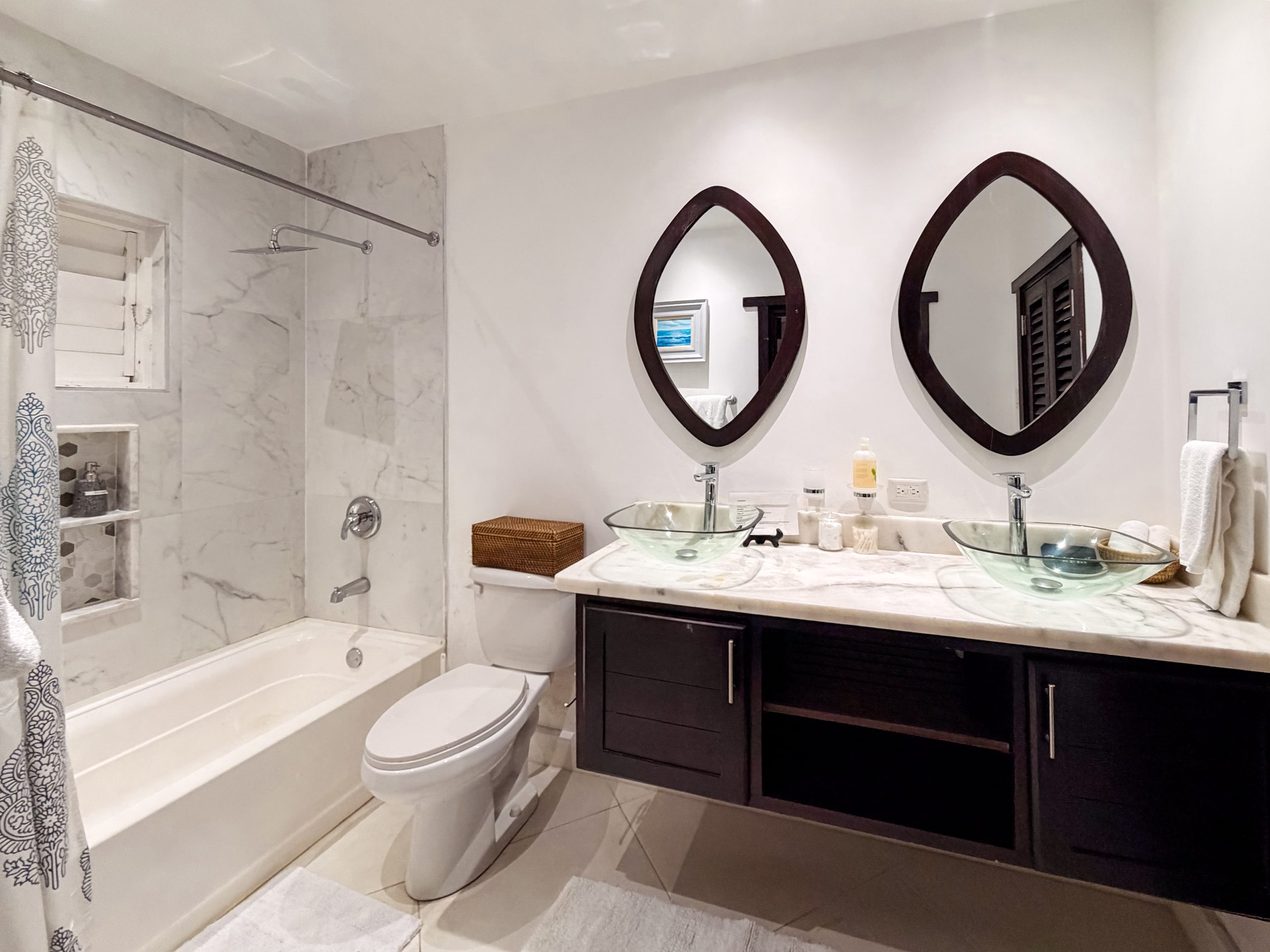 Luxury bathroom in the Ponciana suite at Coconut Cottage with double vanity, glass vessel sinks, marble finishes and a modern bathtub.